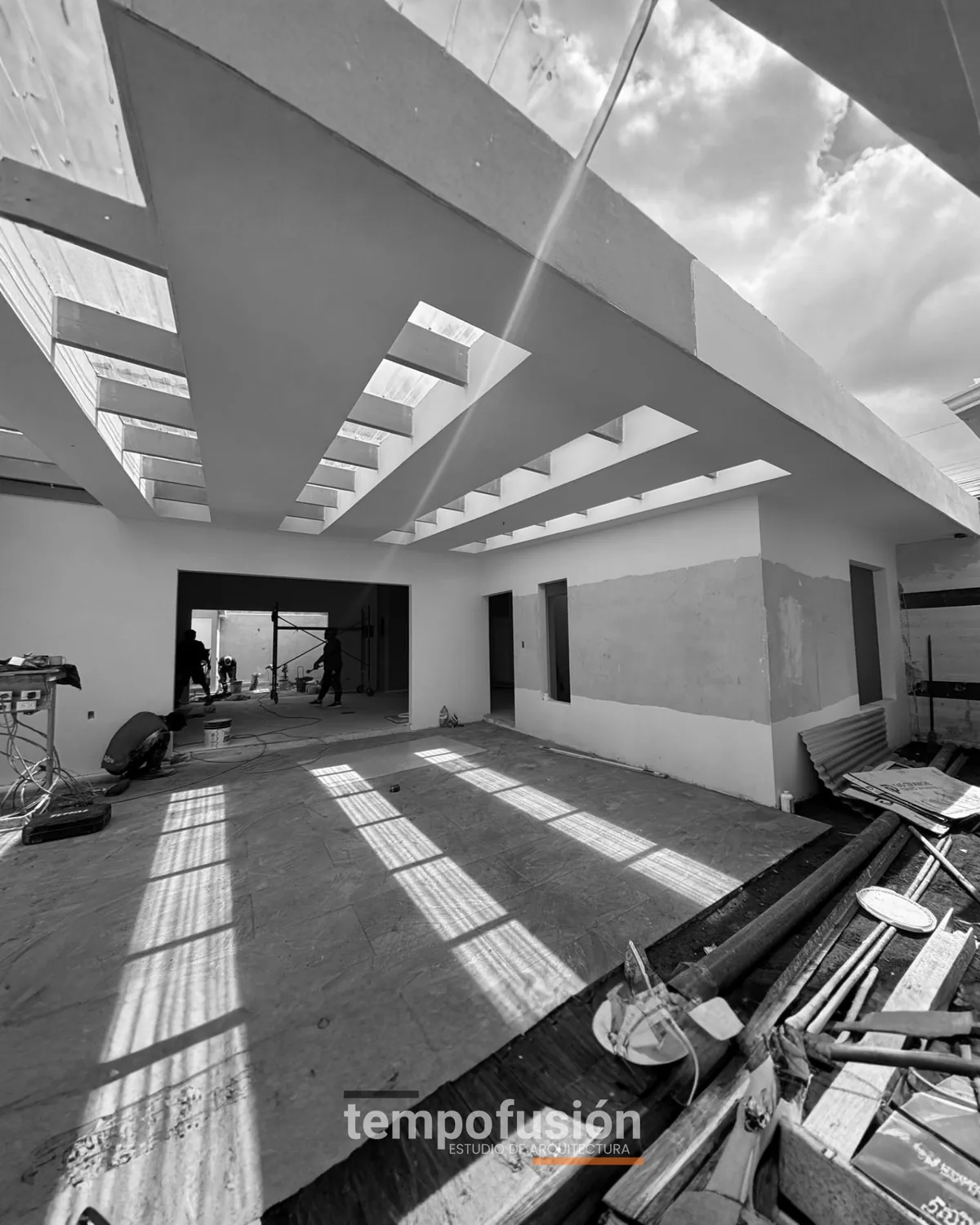 Interior de vivienda en obra gris con luz entrando por el techo, en blanco y negro