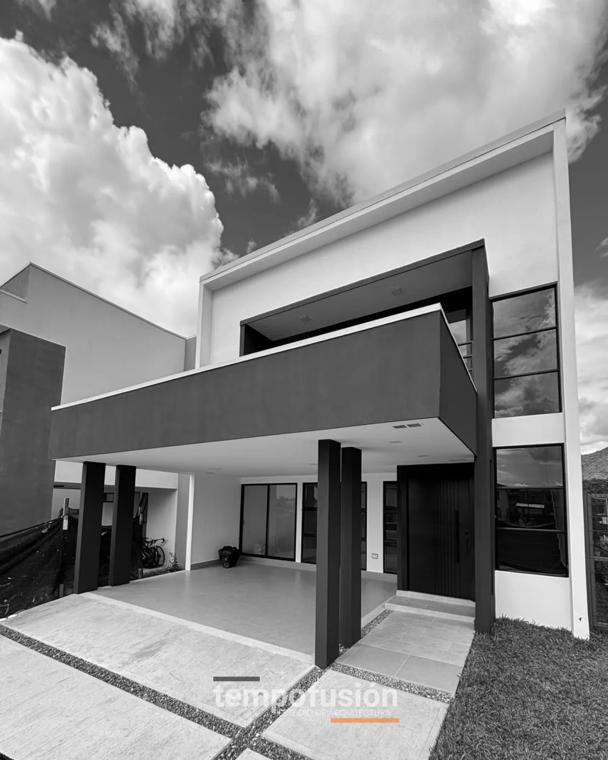 Fachada de dos plantas con volumen saliente y cochera, en blanco y negro